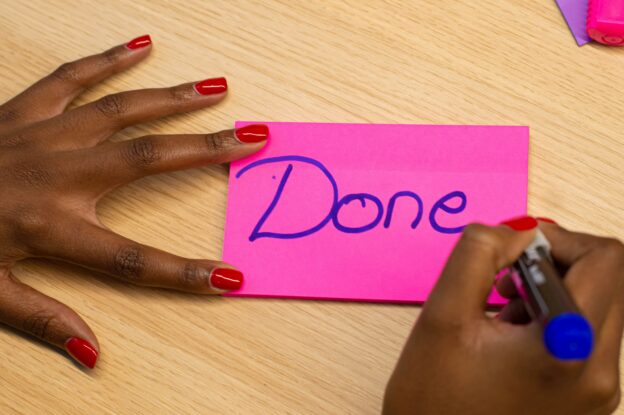 Person writing 'Done' on pink paper with a blue marker for evangelism success.