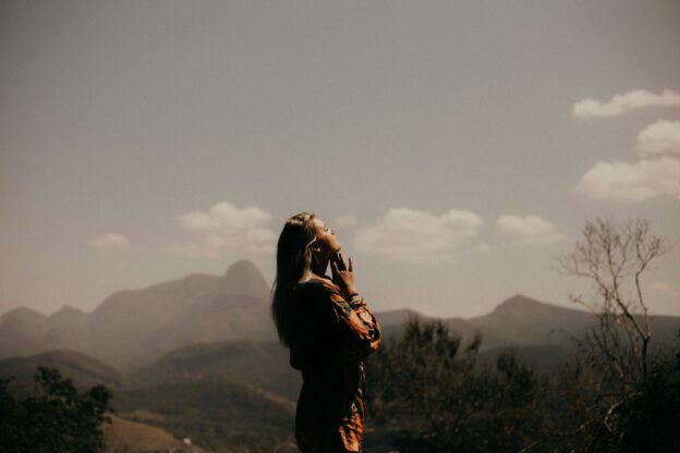 Woman praying outdoors with mountains and sky in the background.