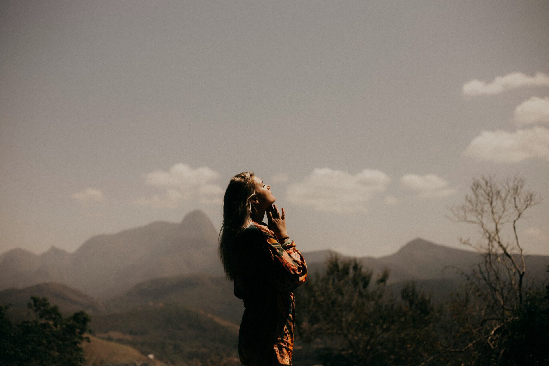 Woman praying outdoors with mountains and sky in the background.