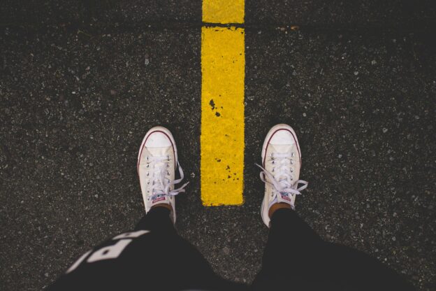 Person standing on street with yellow line, casual footwear, urban scene.