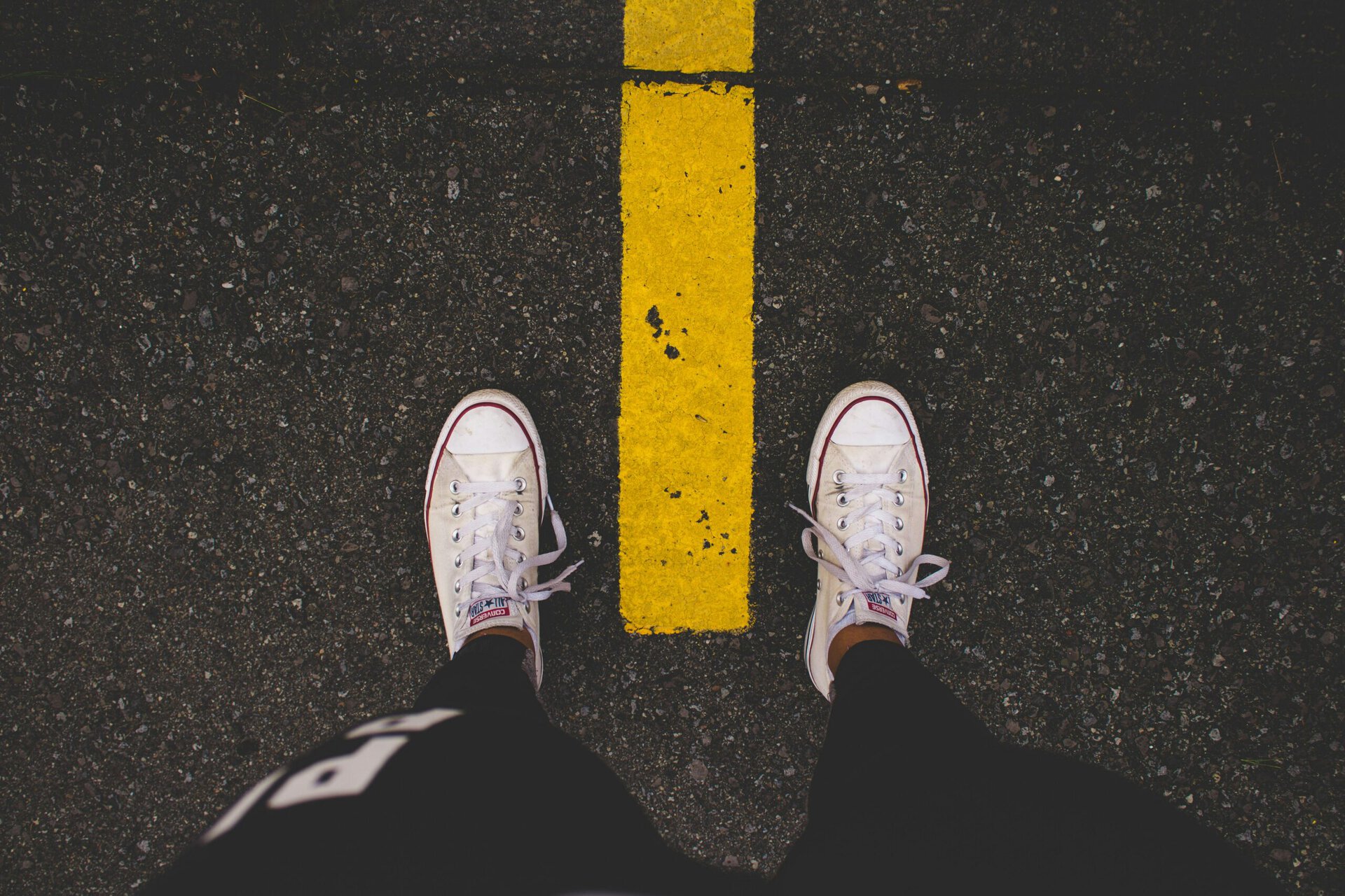 Person standing on street with yellow line, casual footwear, urban scene.