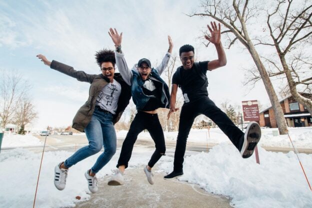 Three young people jumping in snow on a winter day, smiling and having fun.