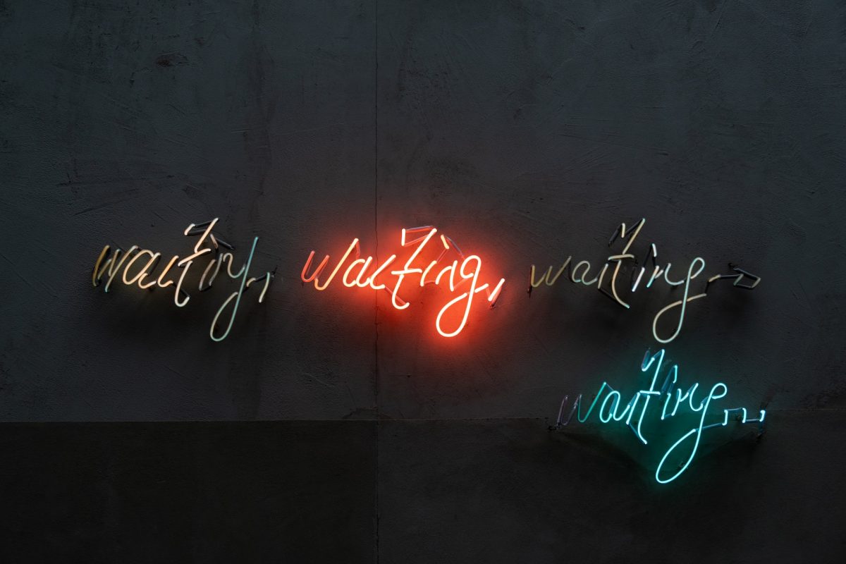 Neon signs in different brightness and colors repeat the word waiting against a dark background