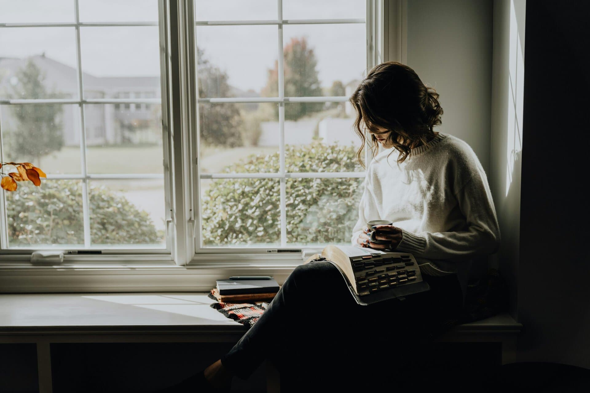 Young woman reading and using her phone by the window.