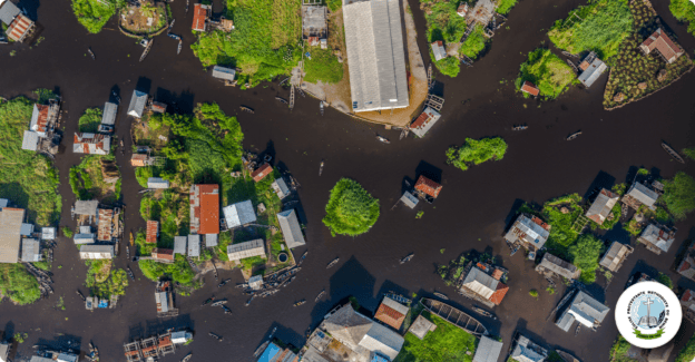 Aerial view of a flooded neighborhood with houses and trees, representing community outreach and res.