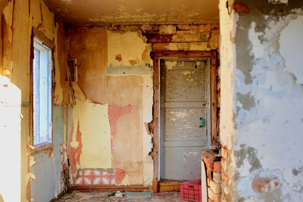 Abandoned room with peeling paint, broken walls, and a closed door.