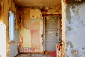Abandoned room with peeling paint, broken walls, and a closed door.